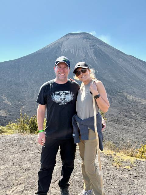       Hikers standing on dark volcanic slope with rocky cone towering above them
  