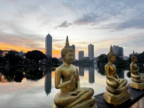       Golden Buddha statues overlooking a lake with Colombo’s modern skyline at sunset
  