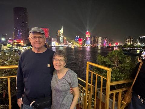       Couple posing on a riverside deck with the illuminated Ho Chi Minh City skyline behind them at night
  