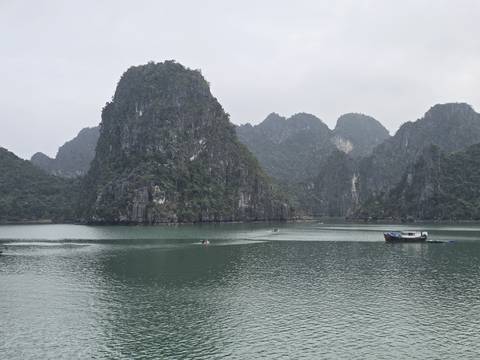       Towering limestone karsts rise from calm green waters in misty Ha Long Bay
  