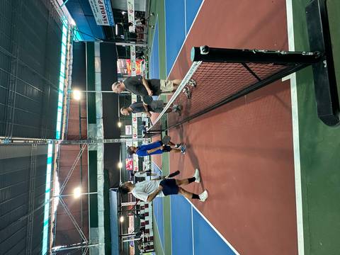       Players shaking hands across an indoor pickleball court net under bright lights
  