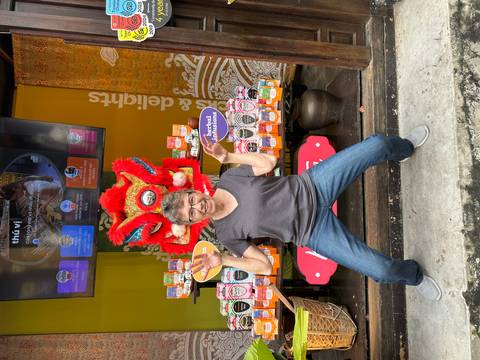       Traveler posing energetically with a vibrant red lion-dance head outside a spice and tea shop
  
