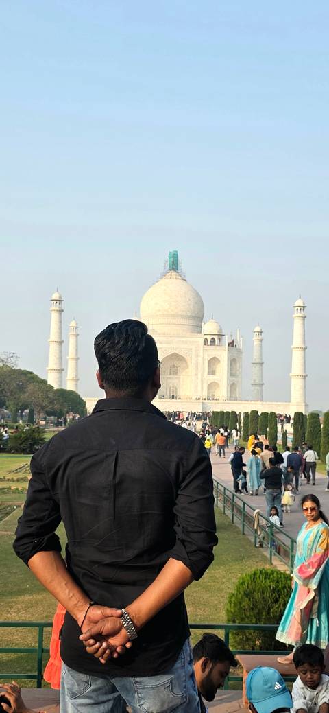      Traveler gazing at the front of the Taj Mahal from the garden pathway on a hazy morning.
  
