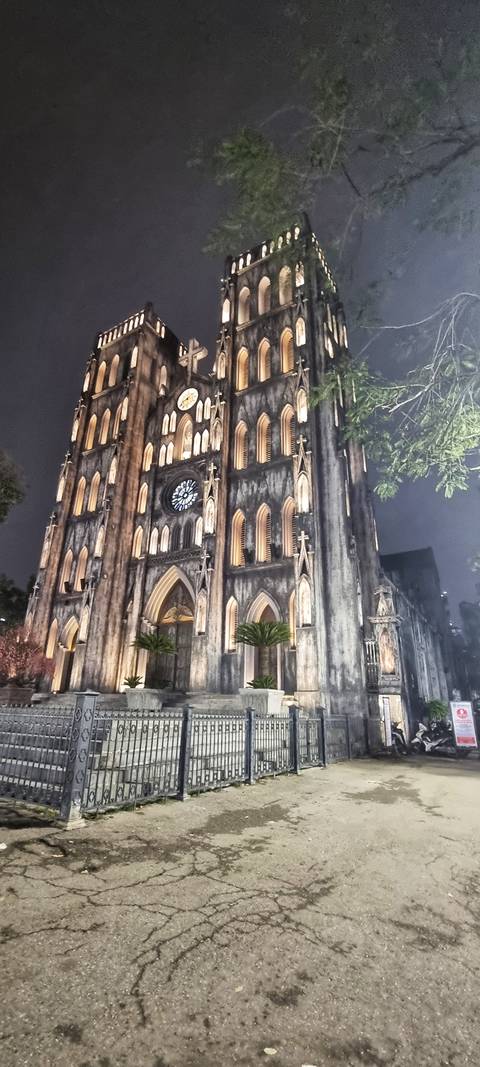       Neo-Gothic cathedral facade illuminated at night with pointed arches and a large rose window.
  