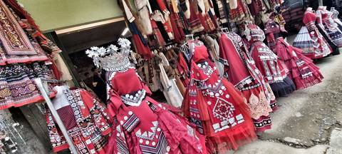       Rows of bright red ethnic dresses and textiles displayed outside a hill-town shop.
  