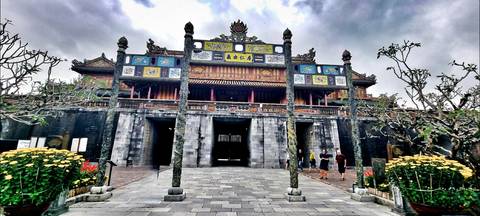       Grand ornamental gate of Hue’s Imperial City with carved pillars and colorful panels, visitors walking on the stone courtyard.
  
