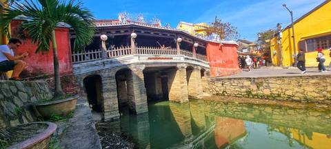       Historic Japanese Covered Bridge crossing a narrow canal in Hoi An’s old town under bright skies.
  