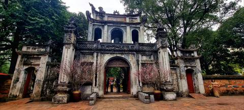       Ancient stone gateway of Hanoi’s Temple of Literature framed by trees and flowering branches.
  