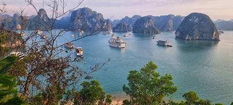       Panoramic view of emerald waters and cruise boats scattered among towering limestone islands of Halong Bay.
  