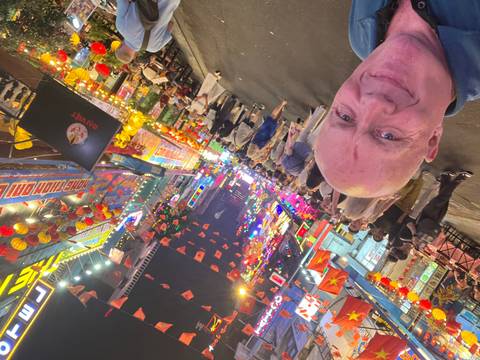       Selfie in a neon-lit night market street bursting with flags, signs, and festive crowds
  