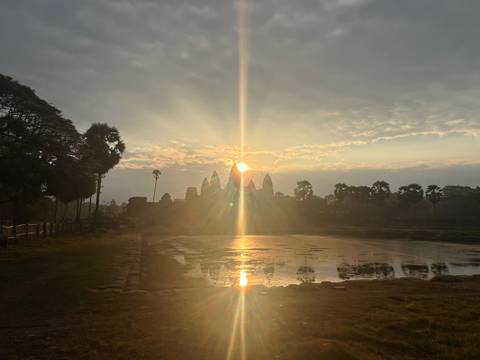       Golden sunrise breaking over the silhouette of Angkor Wat, reflections shimmering in still water
  