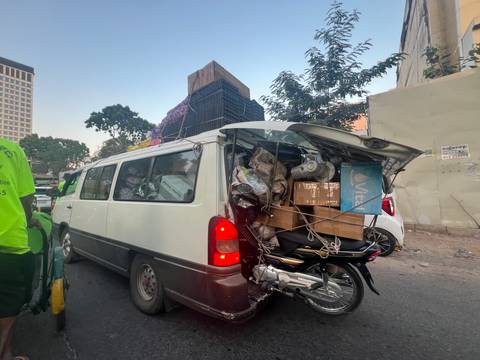       Overloaded white van piled with boxes, motorbike, and crates tied on the open rear hatch in traffic
  