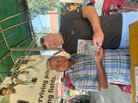       Tourist and local author proudly holding a book together at an outdoor stall shaded by green tarp
  