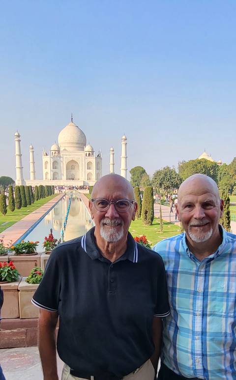       Two smiling men pose in front of the Taj Mahal and reflecting pool on a clear morning
  