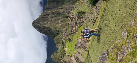       Couple poses on a grassy ledge overlooking Machu Picchu and Huayna Picchu peak
  