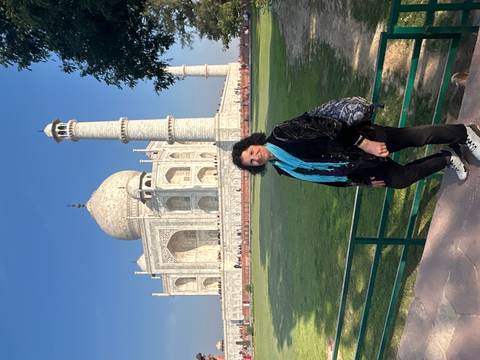       Woman poses near railing with full view of Taj Mahal and minaret behind her
  
