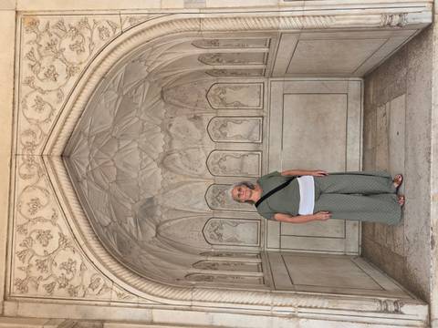       A woman poses inside an ornately carved marble alcove of a Mughal-era fort or palace.
  