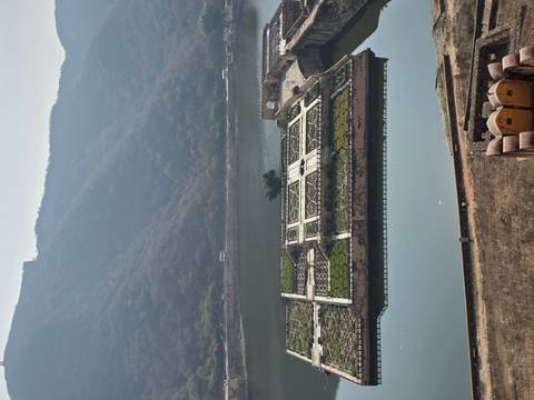       Elevated view of patterned garden islands and a calm lake surrounded by forested hills.
  