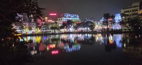       Nighttime cityscape with colourful neon reflections on a tranquil lake in Hanoi.
  