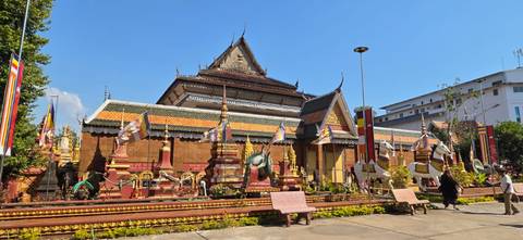       Colourful Cambodian pagoda complex with ornate stupas under a clear blue sky.
  