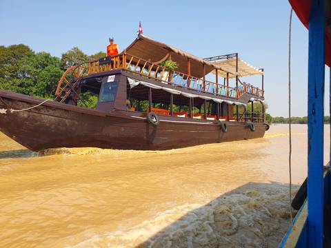       Traditional wooden cruise boat speeds along muddy waters of the Mekong Delta.
  