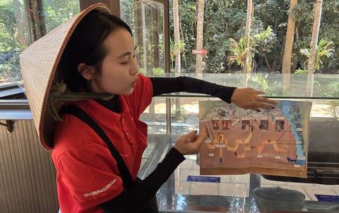       Guide demonstrates a Cu Chi tunnels diagram to visitors inside a forest exhibit.
  