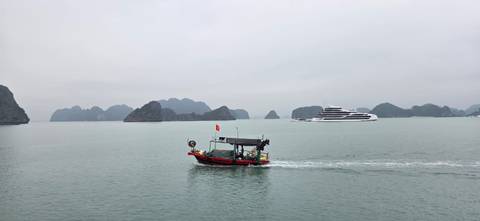       Small fishing boat passes a luxury cruise ship amid misty limestone islands of Halong Bay.
  