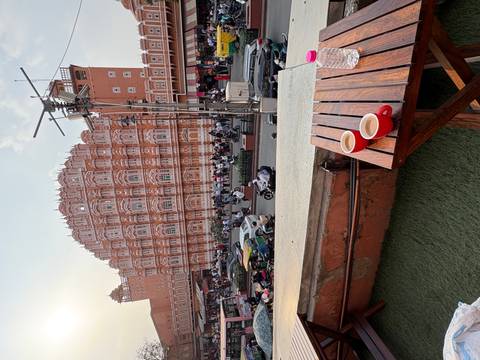       Street-level view of Jaipur’s ornate Hawa Mahal with bustling traffic and two cups of chai in foreground.
  