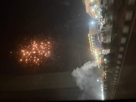      Blurry night scene of fireworks exploding above a busy street with smoke.
  