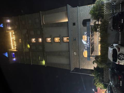       Tall modern hotel building lit at night with cars parked in front.
  