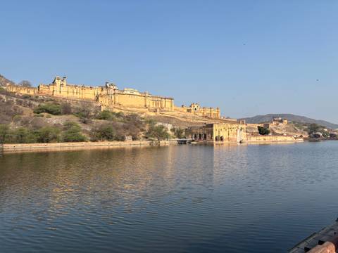      Amber Fort’s yellow sandstone walls rise above a tranquil lake reflecting the structure.
  