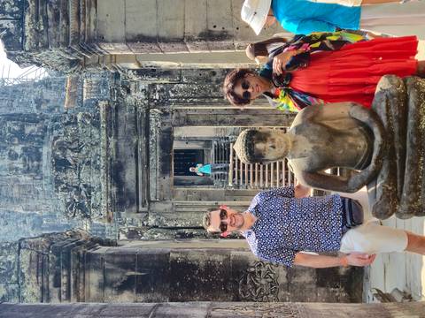       Visitors stand beside a weathered Buddha statue at Bayon Temple's intricately carved stone entrance
  