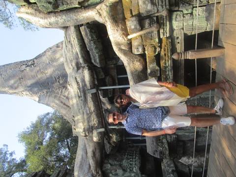       Couple poses before the giant silk-cotton tree roots enveloping Ta Prohm temple stones at Angkor
  