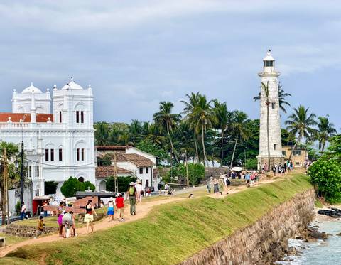       Crowds explore Galle Fort’s white lighthouse and colonial buildings framed by tropical palms
  