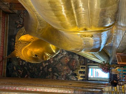       Golden Reclining Buddha inside richly decorated temple hall.
  