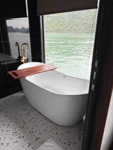       Modern freestanding bathtub on a deck with view onto calm green water.
  