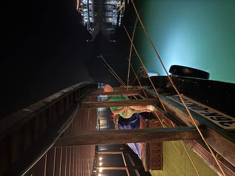       Man stepping off a wooden junk boat at night, green light illuminating the calm water in Halong Bay.
  