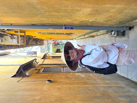       Cheerful guide wearing a conical hat poses in a narrow yellow-walled alley in Hoi An.
  