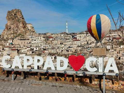       Large sign reading “CAPPAD♥CIA” overlooks the stone houses and mosque of Göreme.
  