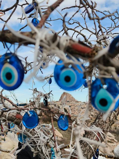       Blue evil eye charms hang from branches, with Uchisar Castle blurred in the background.
  