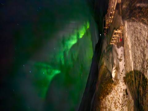       Vertical panorama of green aurora over snowy valley with camper vans and picnic tables
  