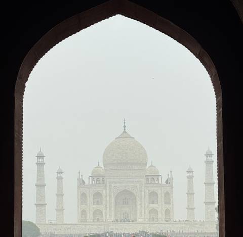       Hazy view of the Taj Mahal framed by a dark archway.
  