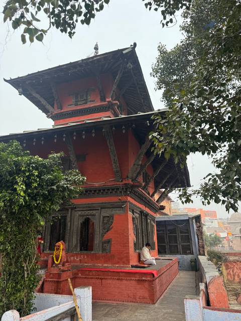       Red brick pagoda-style temple partially framed by foliage on a hazy day.
  