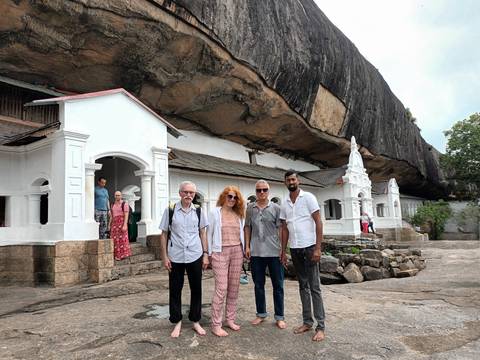       Tourists pose in front of white-walled cave temples set beneath a massive rock overhang in Sri Lanka.
  