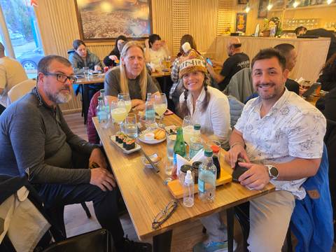       Friends enjoy a meal together at a wooden restaurant table with sushi and drinks.
  