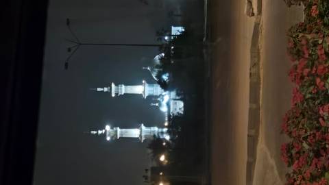       Nighttime view of an illuminated mosque with twin minarets seen across a quiet road.
  
