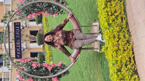       A smiling woman sits on a decorative swing ringed with flowers in a manicured resort garden.
  