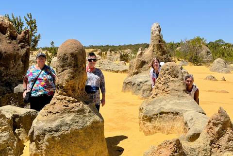       Travellers smiling and posing among tall limestone formations in the Pinnacles Desert
  
