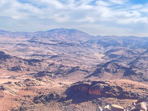       Expansive view over rugged, barren mountains and desert valleys beneath a clear blue sky.
  