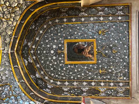       Intricate mirrored and floral inlay wall with a small central mirror reflecting the photographer.
  